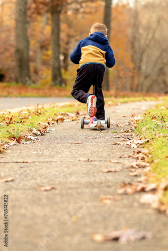 Young Boy Riding Scooter on Sidewalk in the Fall photo