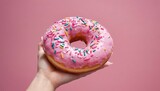 Pink donut being held up by a womens hand