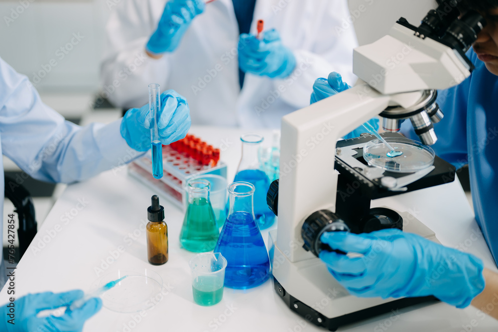 Team scientists conducting research investigations in a medical laboratory, a researcher in the foreground is using a microscope in laboratory Team scientists conducting research investigations in a medical laboratory, a researcher in the foreground is using a microscope in laboratory