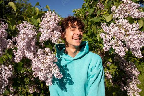 Portrait of a handsome young man on a background of lilac flowers. A student poses looking at the camera.
