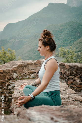 A Woman Achieves Inner Peace through Yoga and Meditation in Lotus Seat, Surrounded by the Tranquil Ambiance of an Old Stone Wall amidst the Lush Greenery of a Forest Backdrop