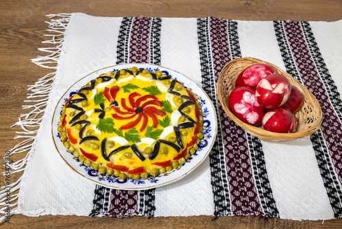 Traditional Romanian boeuf (beef) salad decorated and red Easter eggs with a traditional towel on a wooden table