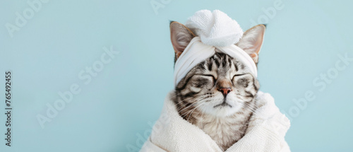 A domestic tabby cat indulges in self-care with a towel wrap and head turban on a gentle beige backdrop