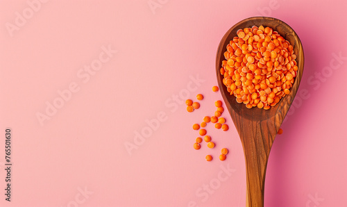 red lentils in a wooden spoon seen from above on a pastel pink background, top view banner with copy 