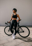 Young woman cyclist in protective gear standing with her bike while training outdoors and looks away