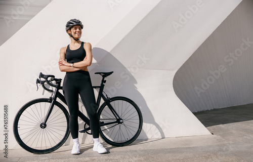Smiling woman cyclist in protective gear standing with her bike while training outdoors 
