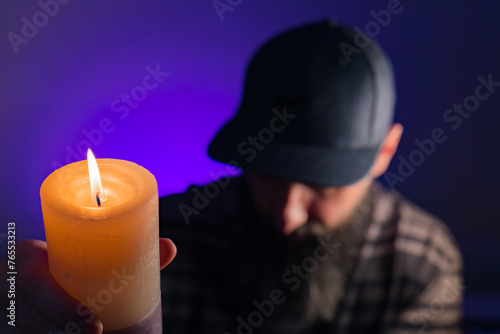 Bearded man holding a lit candle in his hand. Purple background