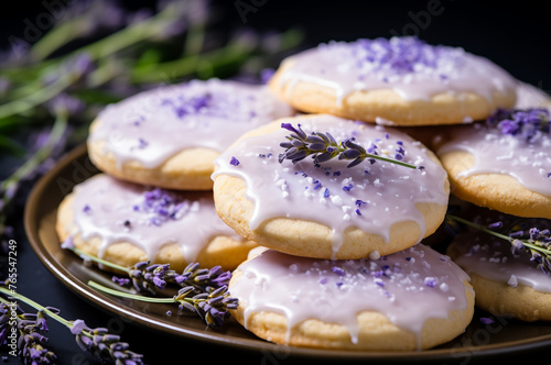 Glazed lavender cookies on a plate with fresh flowers on background. Horizontal, close-up, side view.
