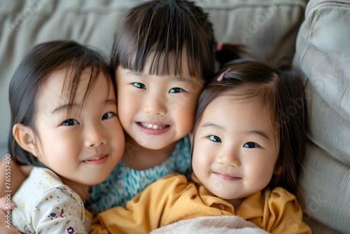 Portrait of three young asian girls hugging each other on the couch indoors