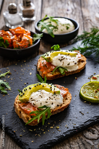 Tasty sandwiches - toasted bread with burrata cheese, smoked salmon, avocado and arugula on wooden table 