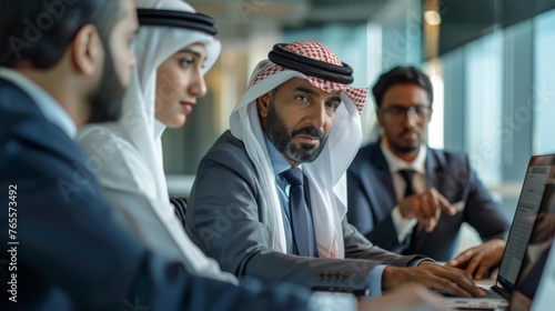 A diverse group of Arab men and women in traditional and formal wear concentrate during a business meeting in a corporate office photo