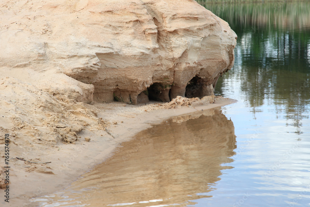 A sandy cliff reflected in the surface of lake water.