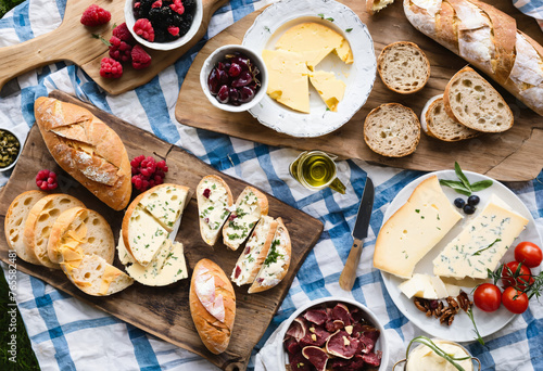 A rustic picnic spread, complete with a crusty baguette, ripe cheeses, and savory meats