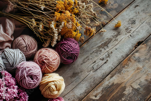 yellow, pink and beige woolen yarn balls and dryed flowers on a rustic wooden ground with space for text