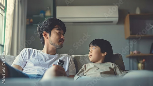 Asain father and a child on the sofa. The child has a TV remote in his hand and the father has an air conditioning remote looking at each other, with the air conditioning behind them
