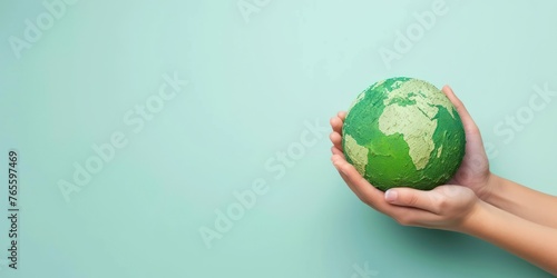 A pair of hands holding a green earth globe against a light blue background, an image fitting for concepts related to global care or environmental education. photo
