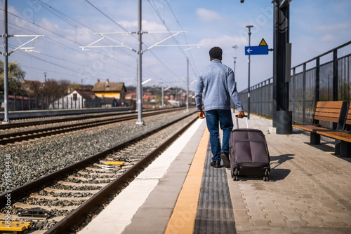 Rear view of man with suitcase walking on railway station. © inesbazdar