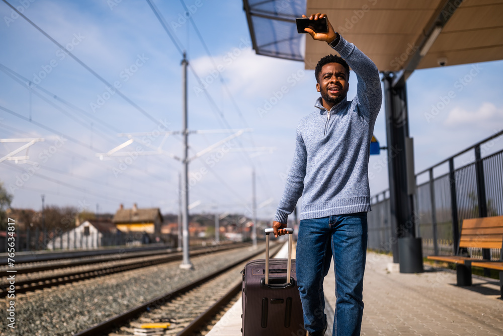 Man waving to a leaving train and running along railway station with suitcase and mobile phone.
