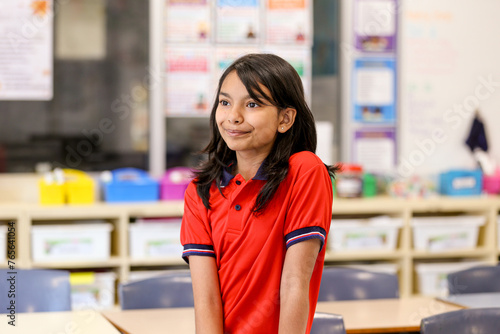 Female school student in a red polo shirt thoughtfully standing in classroom photo