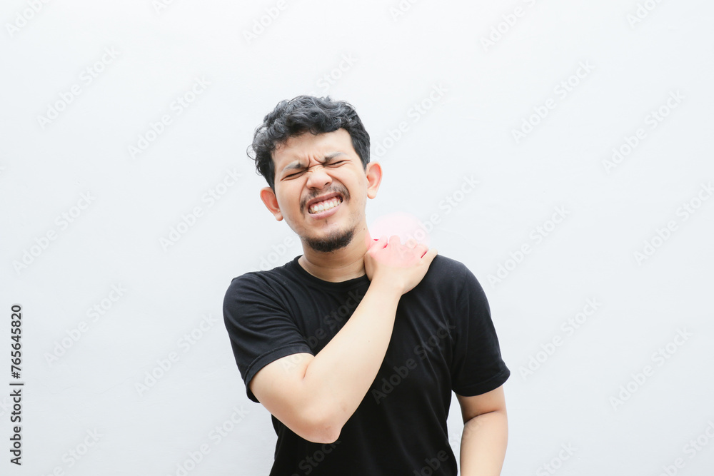 an asian man holds his shoulder and looks in pain an asian man holds his shoulder and looks in pain