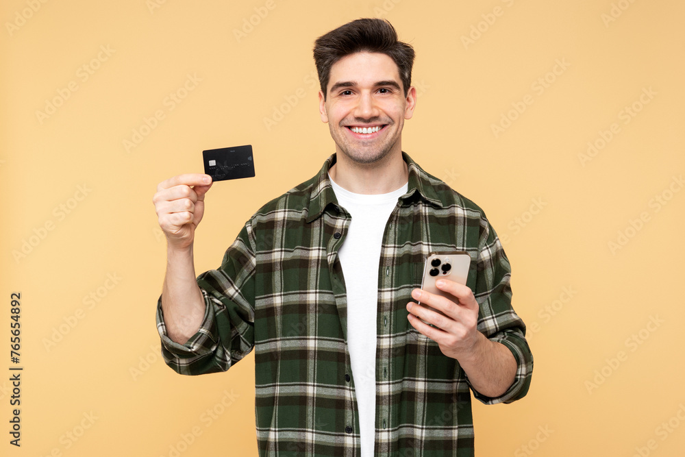 Man with wide smile holding his mobile phone and demonstrating a credit card, looking at the camera Man with wide smile holding his mobile phone and demonstrating a credit card, looking at the camera