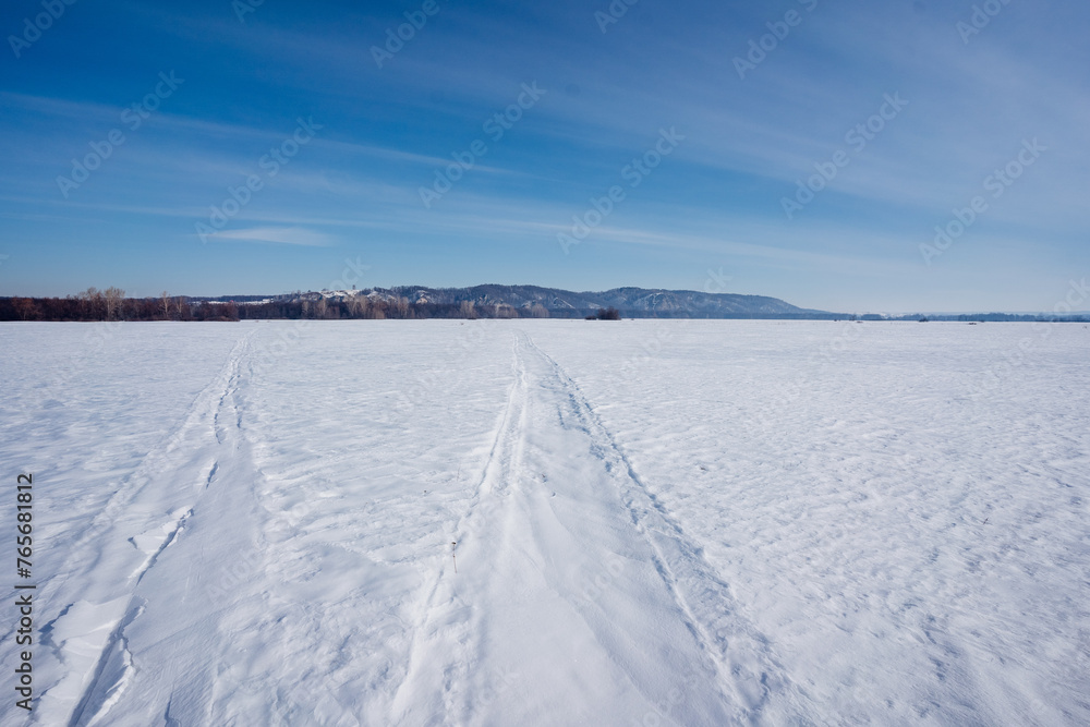 Tire tracks cut through snowy field under cold winter sky
