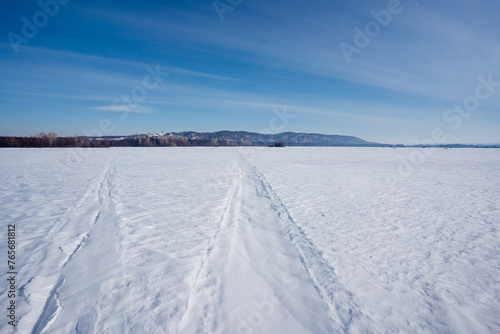 Tire tracks cut through snowy field under cold winter sky