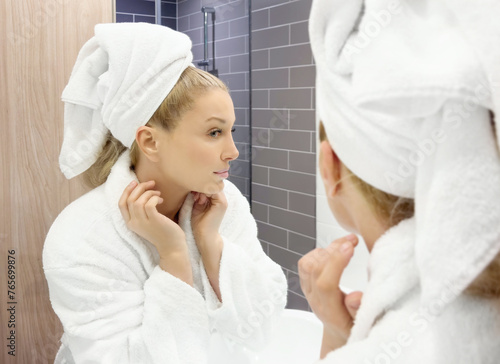 woman looking in the mirror in the bathroom and taking care of her skin.