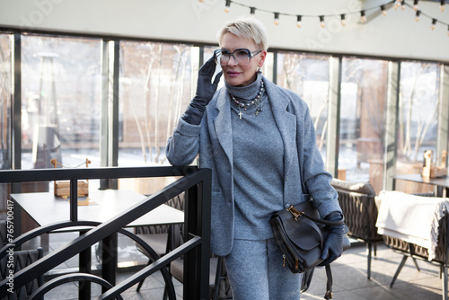 Attractive and stylish mature woman in grey pant suit with jacket and turtleneck, accessorized with handbag. The perfect look for successful women over 50 © Anna Zhuk