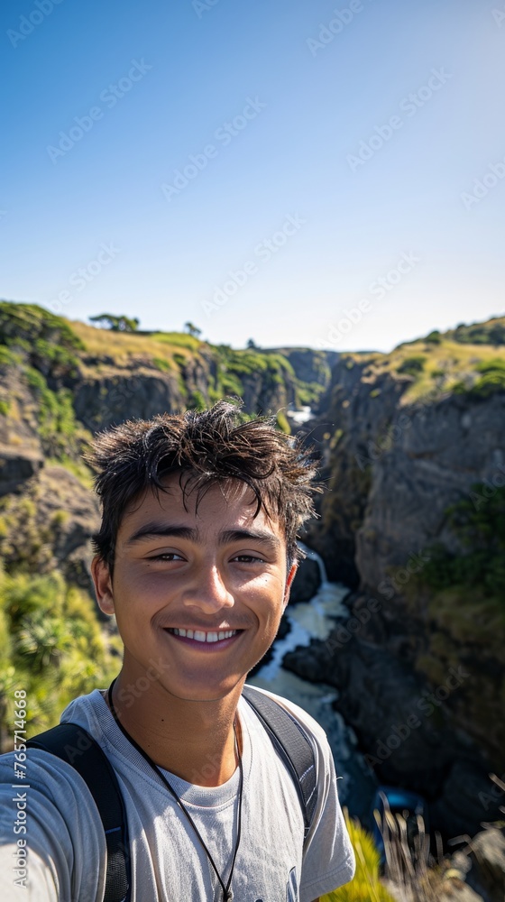 Naklejka premium A young man is smiling and taking a selfie in front of a waterfall