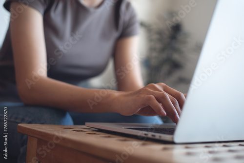 Woman hand typing on laptop computer on wooden table in coffee shop. Female freelancer online working, surfing the internet, working from home, freelance lifestyle, business casual © tippapatt