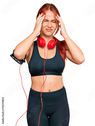 Young redhead woman wearing gym clothes and using headphones suffering from headache desperate and stressed because pain and migraine. hands on head.