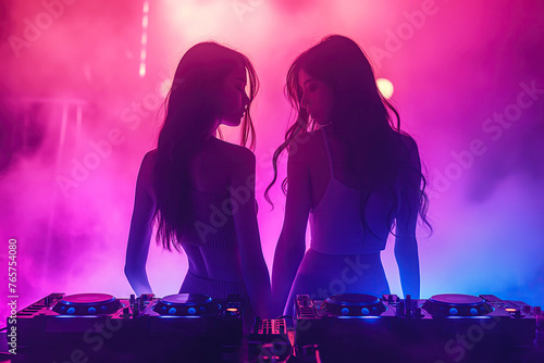 Two sexy go-go girls dancing on stage of a night club at DJ booth with a mixer console