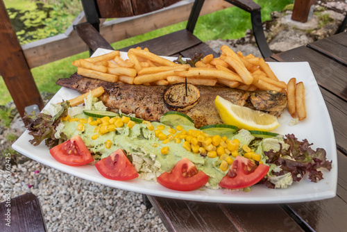 Plate of grilled trout with fries and salad in a restaurant in Kamienczyk village, Poland