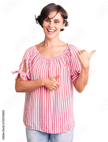 Beautiful young woman with short hair wearing casual summer clothes pointing to the back behind with hand and thumbs up, smiling confident