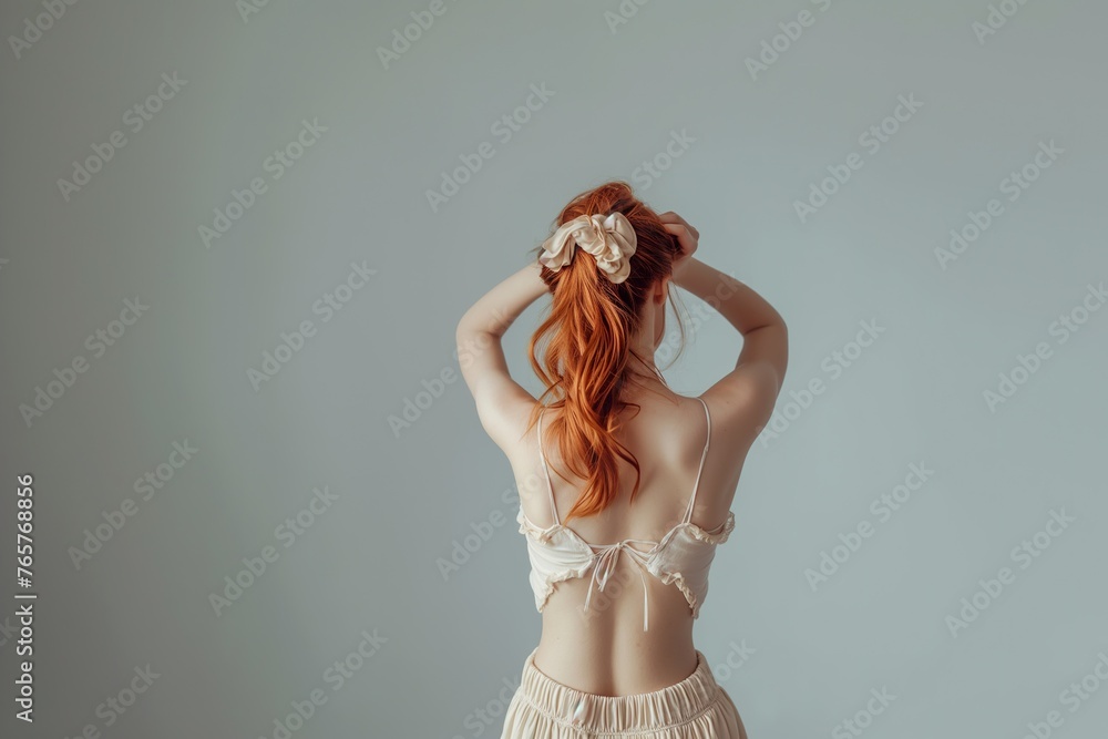 A young woman with red hair is putting a flower in her hair. - obrazy, fototapety, plakaty 