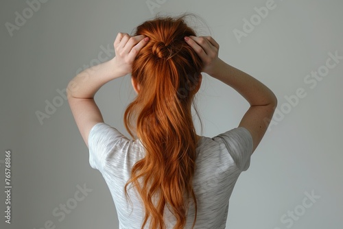 Young woman with red hair tying her long hair into a ponytail using a scrunchy. © Joaquin Corbalan