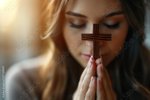 Young woman devoutly holding a cross in her hands against a light background. photo