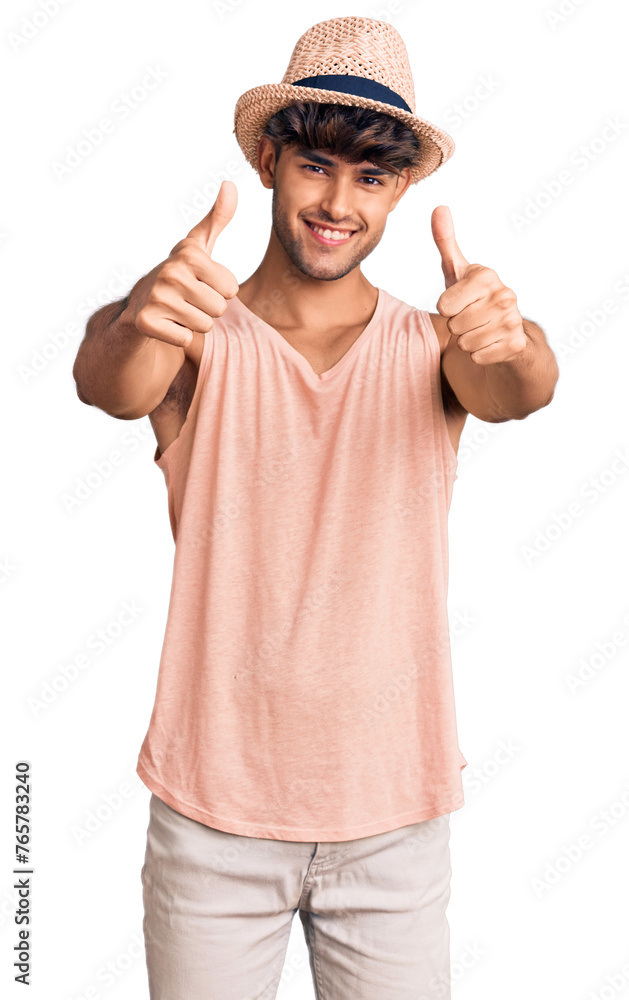 Young hispanic man wearing summer hat approving doing positive gesture with hand, thumbs up smiling and happy for success. winner gesture. Young hispanic man wearing summer hat approving doing positive gesture with hand, thumbs up smiling and happy for success. winner gesture.
