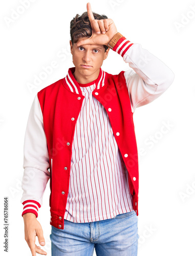 Young handsome man wearing baseball uniform making fun of people with fingers on forehead doing loser gesture mocking and insulting. photo