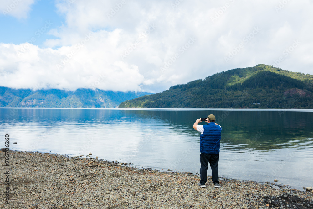 Wide angle shot of Latin Middle-aged Man Enjoying Nature taking a photo with Mobile by Mountain Lake. Copy space