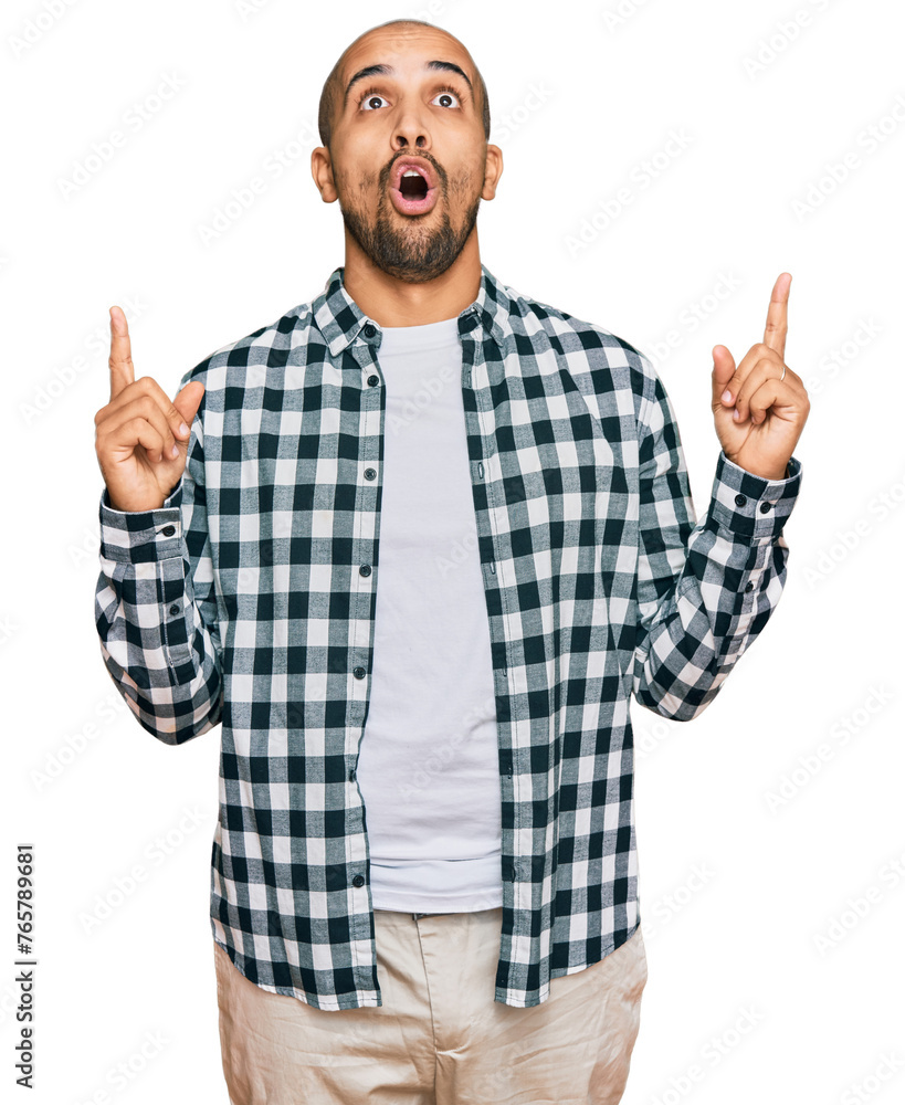 Hispanic adult man wearing casual clothes amazed and surprised looking up and pointing with fingers and raised arms. Hispanic adult man wearing casual clothes amazed and surprised looking up and pointing with fingers and raised arms.