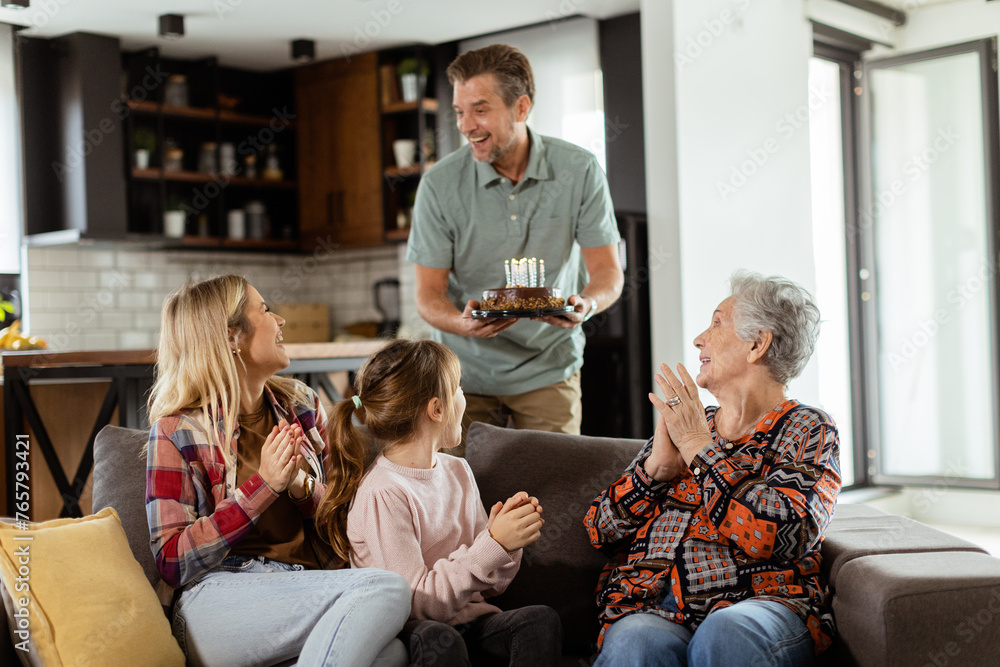 Joyous Family Celebrating Grandmothers Birthday With Cake in a Cozy Living Room Joyous Family Celebrating Grandmothers Birthday With Cake in a Cozy Living Room