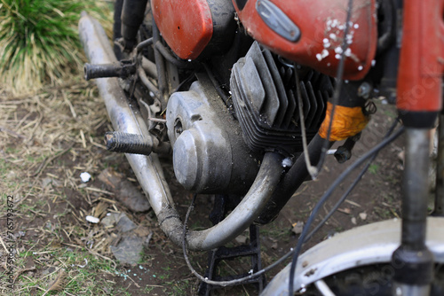 Old motorcycle in the dust. Red retro moto. Defective motorcycle, needs repair. A dirty rural gasoline motorcycle, next to it in the yard around the mess