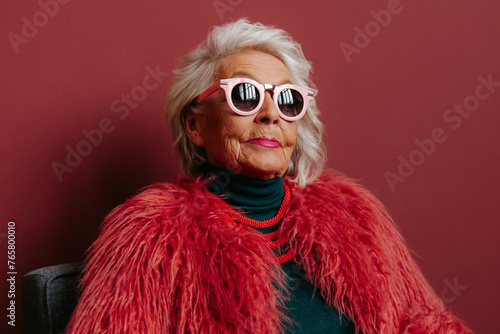 Confident senior woman in fashionable wear looking cool and trendy while sitting against red background
