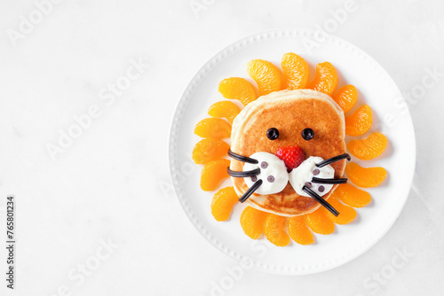 Cute child theme breakfast pancake in the shape of a lion face. Above view on a white marble background.