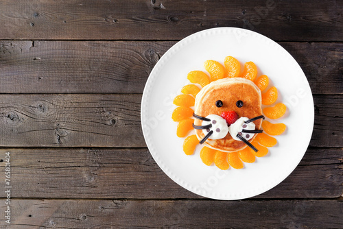 Fun child theme breakfast pancake in the shape of a lion face. Top down view on a dark wood background.