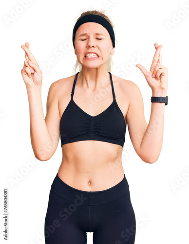 Young beautiful blonde woman wearing sportswear gesturing finger crossed smiling with hope and eyes closed. luck and superstitious concept.