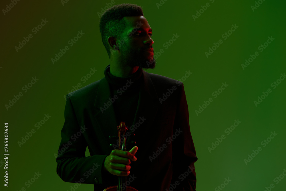 Elegant man in black suit holding a violin against vibrant green and red backdrop Elegant man in black suit holding a violin against vibrant green and red backdrop