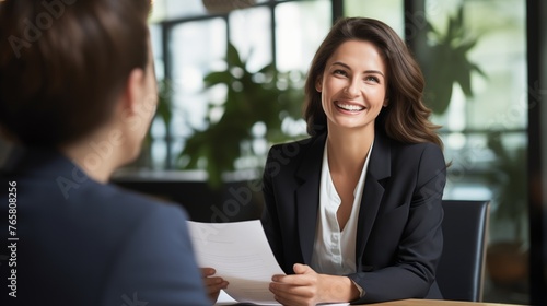This image captures a professional scene in an office where a smiling female financial advisor, attorney, or bank manager is engaged in a business meeting with a client. 